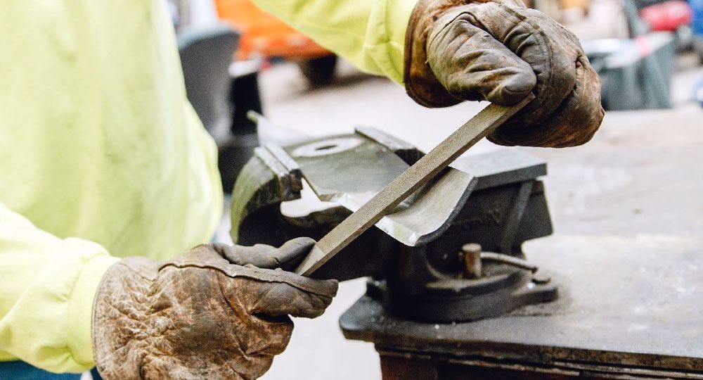 close up of a person at a workbench Sharpening A Mower Blade