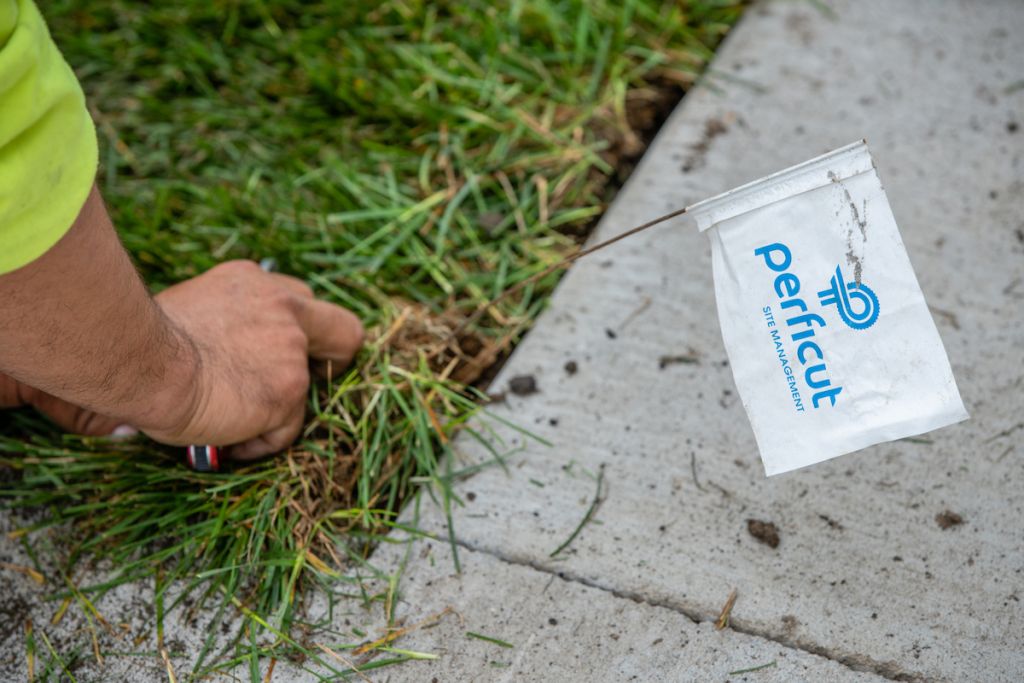Perficut team member putting white and blue Perficut lawn flag in the grass